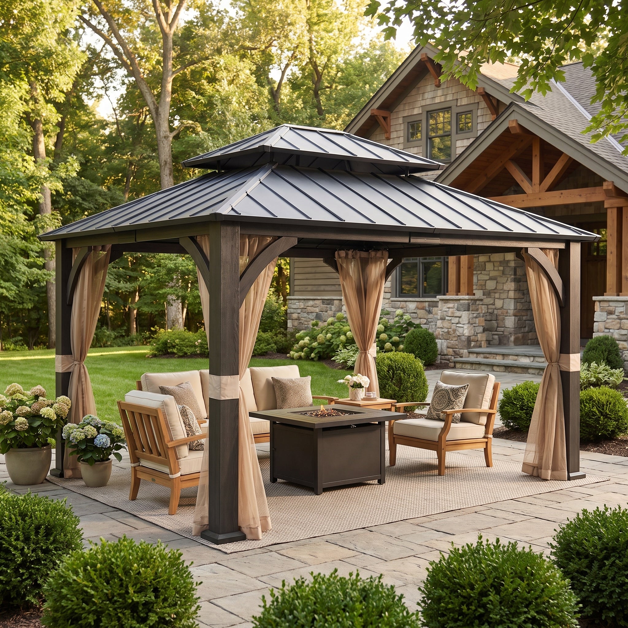A large outdoor gazebo with a dark metal roof and beige curtains frames a patio conversation area with wooden chairs, a fire pit table, and cushions, set in a landscaped backyard with a house in the background.