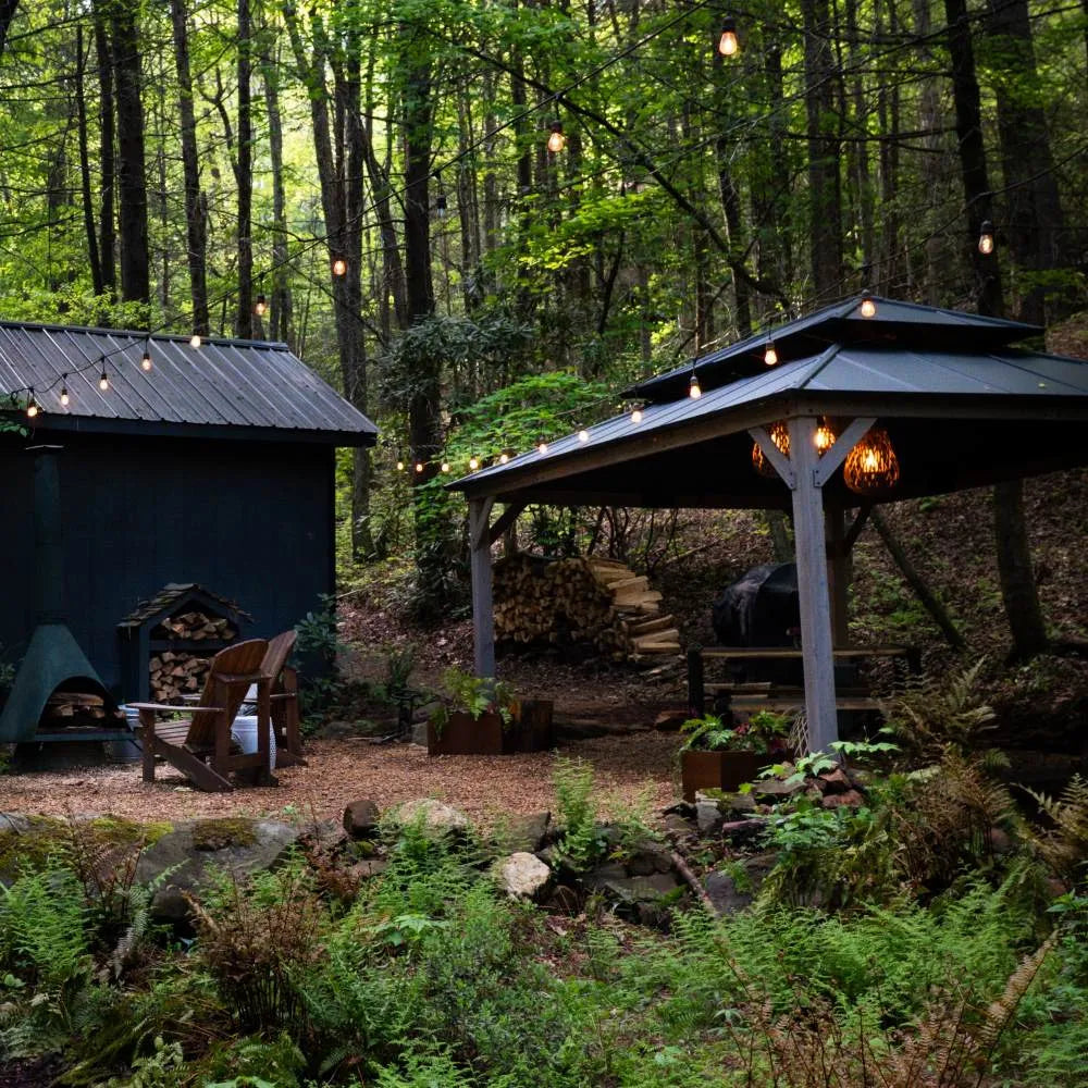 Wooden cabin and gazebo in a forest setting with string lights.