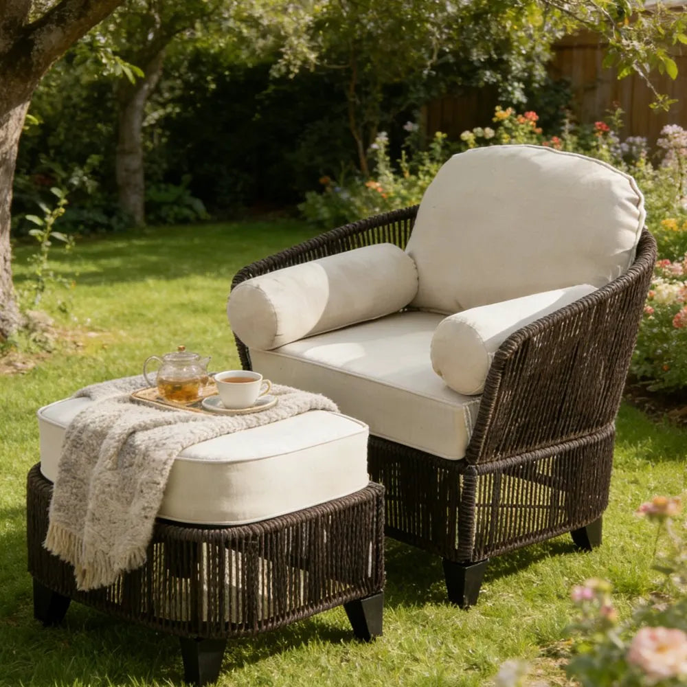 Wicker outdoor chair and ottoman set with cushions in a garden setting.
