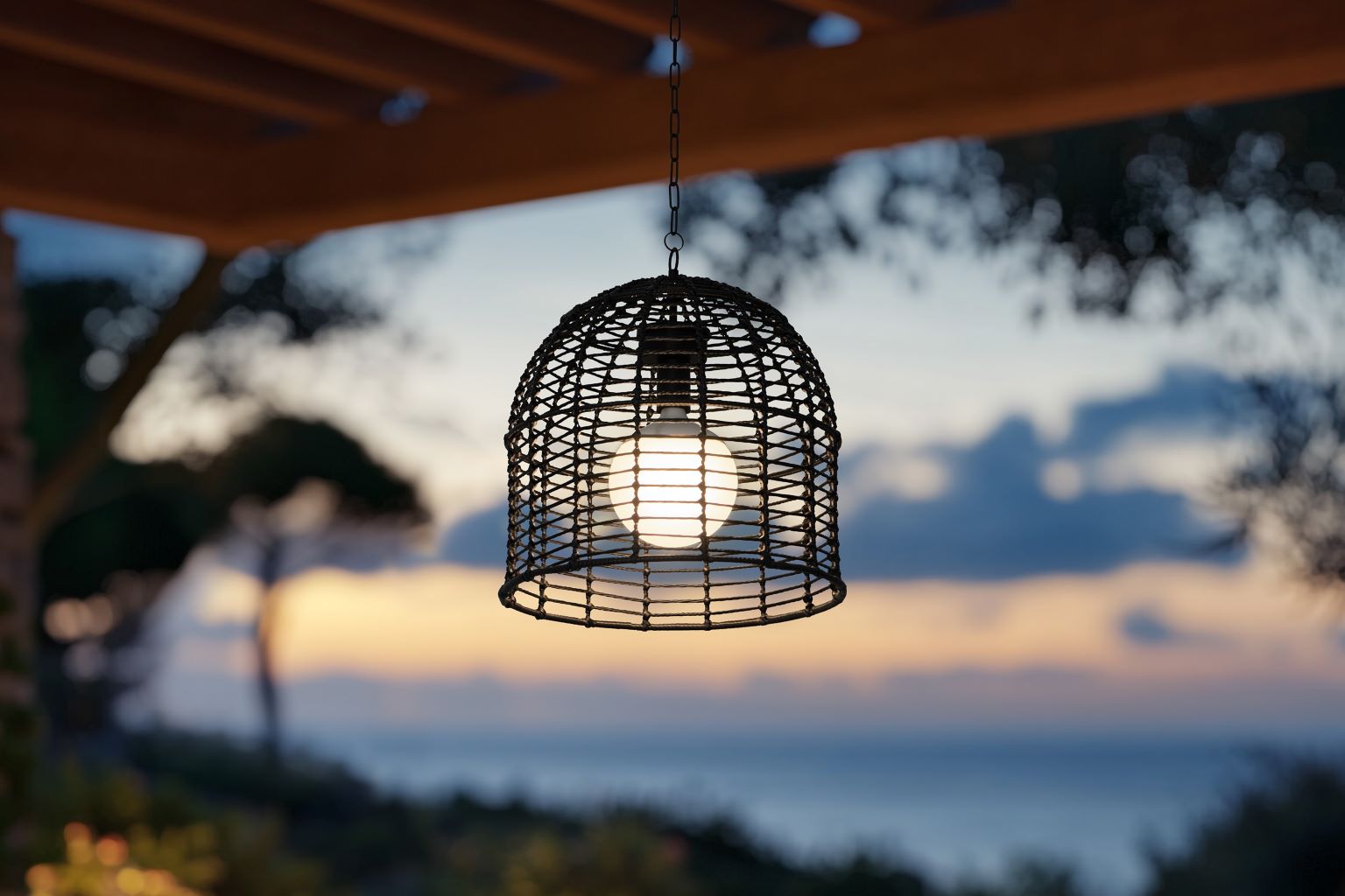 Wicker light fixture hanging under a wooden pergola with a sunset or sunrise in the background.